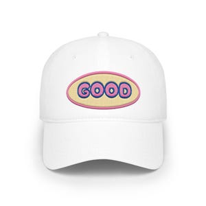 Peut inclure: Casquette de baseball blanche avec le mot "GOOD" brodé en rose et bleu sur un ovale jaune clair. La casquette a une visière incurvée et une couronne arrondie.