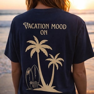Könnte beinhalten: Marineblaues T-Shirt mit Strandmotiv. Auf der Rückseite des Shirts steht der Text "VACATION MOOD ON" über einer Grafik von zwei Palmen und zwei Surfbrettern. Das Shirt wird von einer Person am Strand getragen.