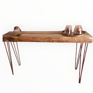 Könnte beinhalten: Ein rustikaler Konsolentisch aus Holz mit Haarnadelbeinen. Die Tischplatte besteht aus Altholz und verfügt über eine dekorative Eulenfigur und ein kleines Tablett mit zwei Gläsern. Die Tischbeine sind aus dunklem Metall.