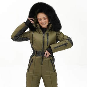 May include: An olive green ski suit with black detailing, a faux fur-trimmed hood, and a belted waist. The one-piece snowsuit has a zip-up front, zipped pockets, and quilted sections. Designed for cold weather, it is suitable for skiing or snowboarding.