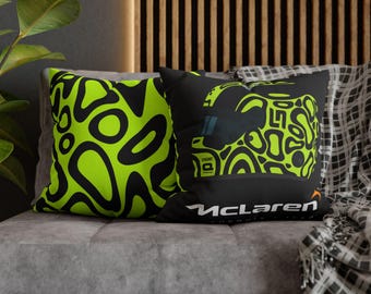 May include: Two decorative throw pillows on a gray couch. One pillow features a neon green and black abstract design. The other pillow has a black background with a neon green helmet design and the McLaren logo.