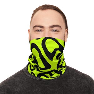 Puede incluir: Un cubrecuello con estampado negro y verde neón. El cubrecuello está envuelto alrededor de la parte inferior de la cara y el cuello. El patrón consiste en grandes formas negras irregulares sobre un fondo verde brillante. La persona lleva una camiseta gris oscuro.