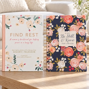 May include: A white book titled Find Rest with floral illustrations next to a dark blue spiral-bound notebook featuring pink roses and the text Ps. 46:10 Be Still, & Know THAT I AM GOD. Both items feature botanical patterns and gold accents.