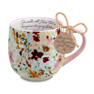 May include: Floral-patterned ceramic mug with a pink handle and rim. The mug features a watercolor design of flowers in shades of red, pink, and yellow. Text on the mug reads "She walks with Jesus. That is her game-changing strategy." A tag reads "strong, brave and capable of great things."