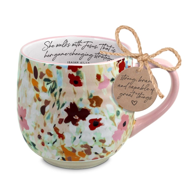 May include: Floral-patterned ceramic mug with a pink handle and rim. The mug features a watercolor design of flowers in shades of red, pink, and yellow. Text on the mug reads "She walks with Jesus. That is her game-changing strategy." A tag reads "strong, brave and capable of great things."