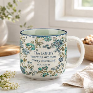 May include: A ceramic mug with a cream-colored base featuring a blue and teal floral pattern. The text "The LORD's mercies are new every morning" and "LAM. 3:22-23" is printed in blue on the front. The mug has a rounded body and a sturdy handle.