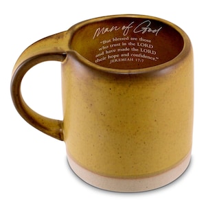 May include: Mustard yellow ceramic mug with a unique handle design. The mug features the text "Man of God" and a Bible verse from Jeremiah 17:7. The base of the mug is a light beige color.