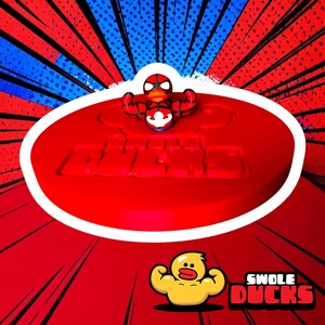 May include: A red circular display base featuring the embossed text SWOLE DUCKS, topped with a small red and black muscular duck figurine wearing a mask. A yellow muscular duck graphic and the text SWOLE DUCKS appear in the lower right corner.