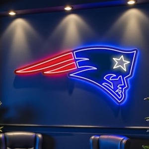 May include: A neon sign of the New England Patriots logo illuminates a dark blue wall. Two black leather armchairs face a small red table. Potted plants and a dark wood floor complete the scene.