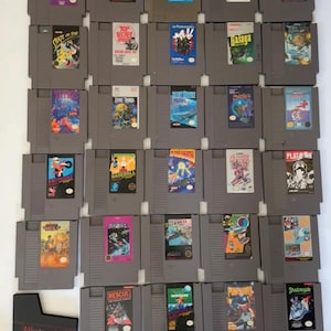 Puede incluir: Una colección de treinta y una cartuchos de juego rectangulares grises para Nintendo Entertainment System dispuestos en una cuadrícula, cada uno con una etiqueta colorida única con títulos como Tetris, Galaga y Excitebike, además de un cartucho negro.
