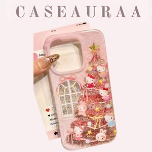 Puede incluir: Una funda de teléfono rosa con un diseño de árbol de Navidad con personajes de Hello Kitty y purpurina. La funda tiene un diseño de ventana con purpurina y el texto "CASEAURA A" en la parte superior.