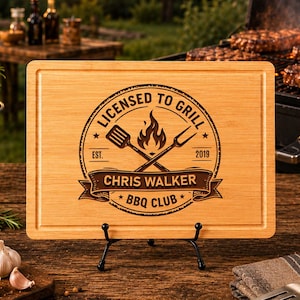 May include: A rectangular bamboo cutting board featuring a laser-engraved design with the text LICENSED TO GRILL, CHRIS WALKER, and BBQ CLUB. The graphic includes a flame icon, a spatula, and a fork, with the established date 2019.