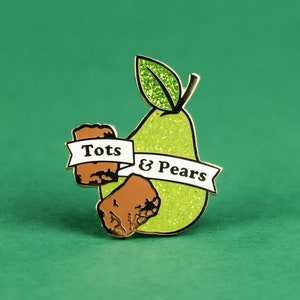 May include: Gold-tone enamel pin featuring a green pear with a white banner that reads "Tots & Pears". The pear is surrounded by two brown, textured,  tots.