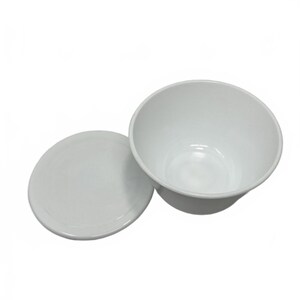 May include: A plain white ceramic bowl with a matching circular lid placed beside it. The bowl has a smooth, glossy finish and a wide, open top, while the lid is flat and round, designed to fit the bowl. Both items are solid white in color.