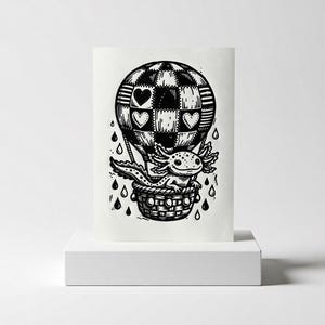May include: Black and white illustration of an axolotl in a hot air balloon. The balloon has a patchwork design with heart shapes. The axolotl is in a woven basket, with rain drops falling around it.
