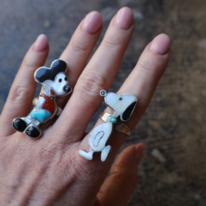 Peut inclure: Deux bagues en argent avec des incrustations de pierres. L'une repr&eacute;sente une souris de dessin anim&eacute; avec des pierres noires, blanches, rouges et turquoise. L'autre repr&eacute;sente un chien blanc avec des oreilles noires et une pierre turquoise.
