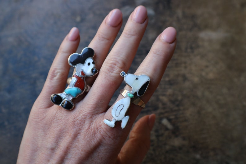 Peut inclure: Deux bagues en argent avec des incrustations de pierres. L'une repr&eacute;sente une souris de dessin anim&eacute; avec des pierres noires, blanches, rouges et turquoise. L'autre repr&eacute;sente un chien blanc avec des oreilles noires et une pierre turquoise.