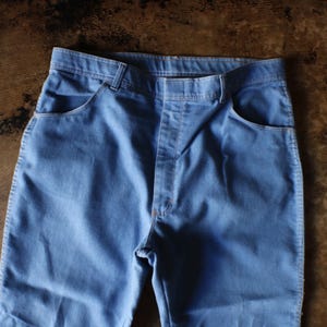 May include: Light blue denim pants with classic five-pocket design. The pants have a straight leg cut and a button and zipper closure. The fabric appears to be a medium-weight denim.