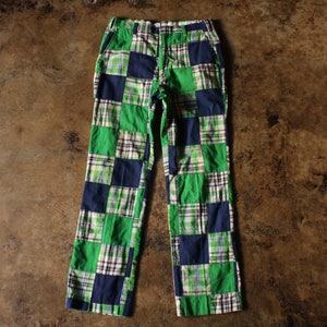 May include: Green, navy, and white plaid patchwork pants. The pants have a straight leg cut and a button and zipper closure. The patchwork design features squares of varying plaid patterns in shades of green, navy, and white.
