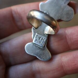 Peut inclure: Une bague en argent dot&eacute;e d'un anneau lisse et arrondi ainsi que d'une monture allong&eacute;e aux formes organiques. Le dessous de la bague pr&eacute;sente une plaque de poin&ccedil;on rectangulaire grav&eacute;e du texte EYM ZUNI en lettres capitales, centr&eacute;e.