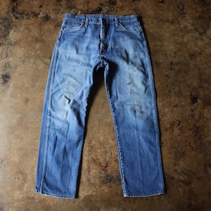 Puede incluir: Vaqueros de mezclilla azul descolorido con un corte recto cl&aacute;sico. Los vaqueros muestran signos de desgaste, con manchas y decoloraci&oacute;n visibles, lo que les da una est&eacute;tica vintage. Los vaqueros est&aacute;n colocados sobre una superficie marr&oacute;n.