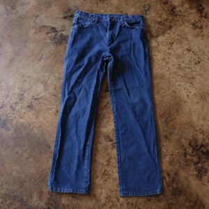 May include: A pair of dark blue denim jeans featuring a classic five-pocket design, a button and zipper fly closure, and a straight-leg cut. The jeans have visible stitching along the seams and pockets, with a standard waistband and belt loops.