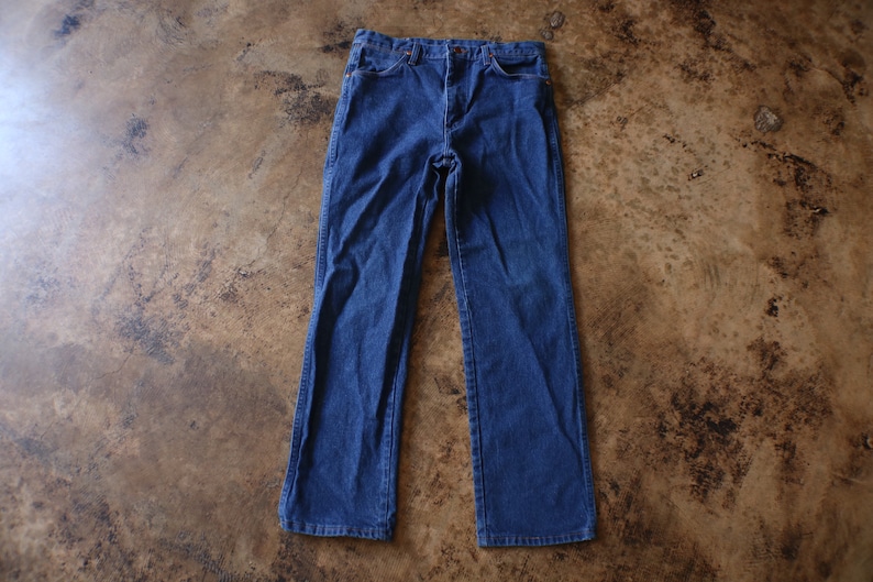 May include: A pair of dark blue denim jeans featuring a classic five-pocket design, a button and zipper fly closure, and a straight-leg cut. The jeans have visible stitching along the seams and pockets, with a standard waistband and belt loops.