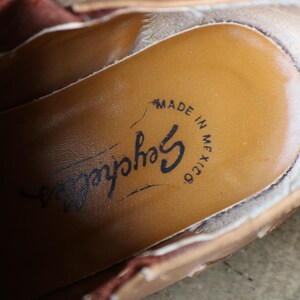May include: Close-up of the inside of a tan leather shoe. The insole is a lighter tan color with the brand name "Seychelles" and the text "MADE IN MEXICO" printed in black ink. The shoe's edges are visible.