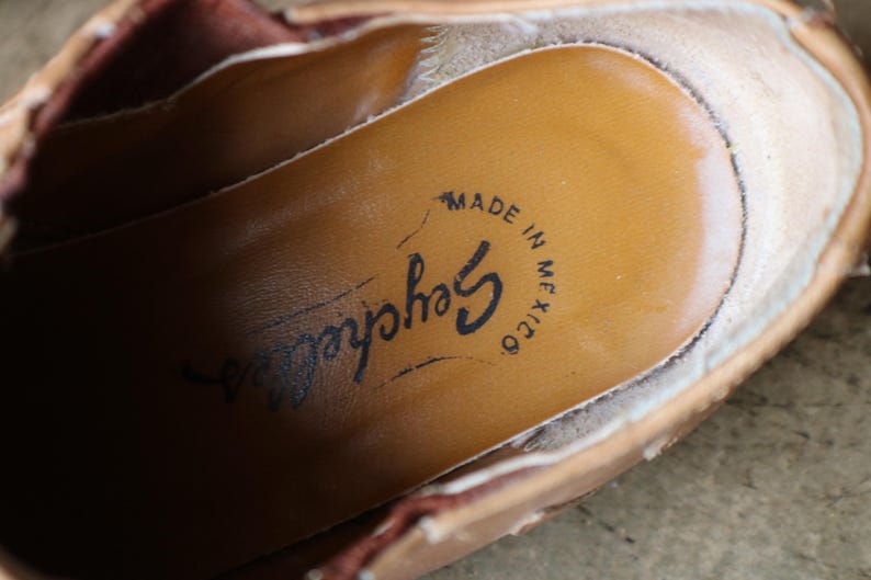 May include: Close-up of the inside of a tan leather shoe. The insole is a lighter tan color with the brand name "Seychelles" and the text "MADE IN MEXICO" printed in black ink. The shoe's edges are visible.
