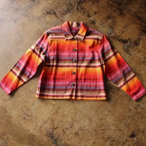 May include: A long-sleeve button-down jacket featuring a horizontal striped pattern in shades of red, orange, yellow, pink, and brown. The jacket includes a standard collar, five front buttons, and two lower patch pockets on the front panel.
