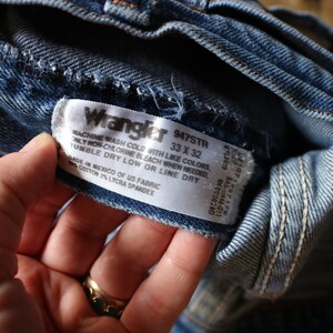 Puede incluir: Primer plano de unos vaqueros Wrangler de mezclilla azul. La etiqueta dice "Wrangler 947STR 33 x 32". La etiqueta tambi&eacute;n incluye instrucciones de lavado y composici&oacute;n de la tela. Los vaqueros est&aacute;n hechos en M&eacute;xico con tela estadounidense, 98% algod&oacute;n y 2% licra spandex.