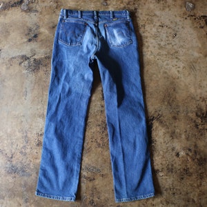 Puede incluir: Vaqueros azules de mezclilla con un dise&ntilde;o cl&aacute;sico de cinco bolsillos. Los vaqueros tienen un lavado descolorido y un corte de pierna recta. Los bolsillos traseros son visibles. Prenda de vestir vintage.