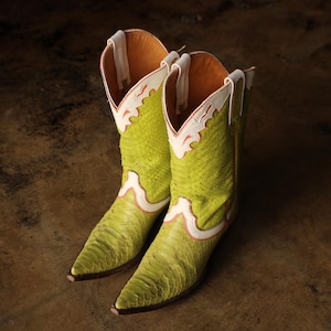 May include: A pair of lime green cowboy boots with a textured pattern. The boots have white and pink accents along the top and a pointed toe. The interior is a warm orange color.
