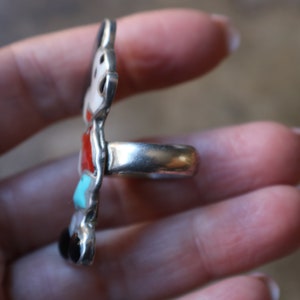 Peut inclure: Une bague en argent avec un motif incrust&eacute; vertical et allong&eacute;. L'incrustation se compose de pierres polies et lisses empil&eacute;es dans des tons de rouge, turquoise, blanc et noir, serties dans une monture en argent poli avec un anneau lisse.