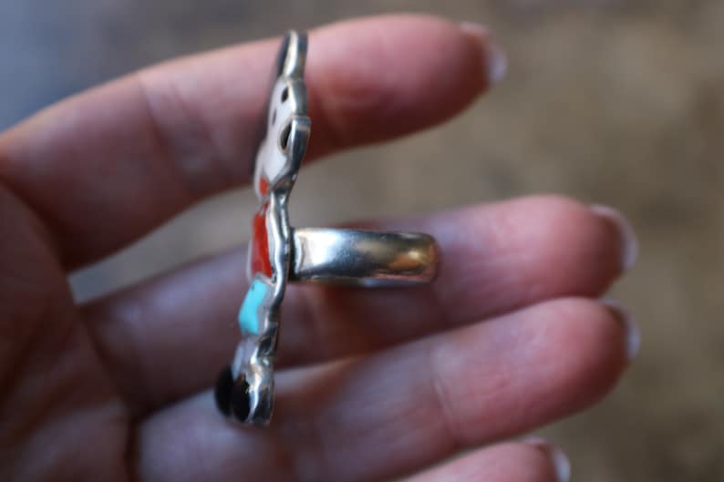 Peut inclure: Une bague en argent avec un motif incrust&eacute; vertical et allong&eacute;. L'incrustation se compose de pierres polies et lisses empil&eacute;es dans des tons de rouge, turquoise, blanc et noir, serties dans une monture en argent poli avec un anneau lisse.