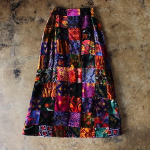 Puede incluir: Una falda larga de patchwork con una variedad de colores y patrones. La falda presenta cuadrados en tonos morado, rojo, naranja, verde y azul. La tela parece ser terciopelo o un material suave similar.