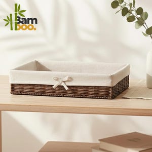 May include: Rectangular woven brown basket with a cream-colored fabric lining and a small bow. The basket is sitting on a wooden shelf. The logo "Bam Boo." is in the upper left corner.