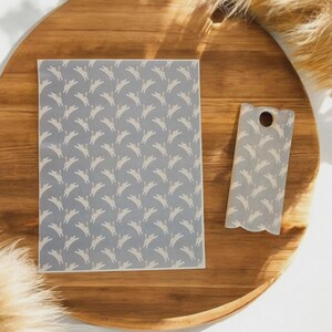 May include: A wooden cutting board with a rectangular placemat and a small, uniquely shaped spatula. Both the placemat and spatula feature a repeating pattern of white rabbit silhouettes on a light blue background. The items are arranged on a wooden surface.