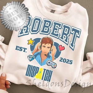 May include: White sweatshirt with a blue and white design featuring the name "ROBERT" and the word "DISPATCH". The design includes a cartoon image of a person wearing a headset, along with pixelated graphics.