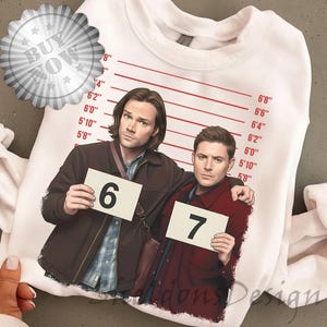 Puede incluir: Sudadera blanca con un gráfico de dos hombres sosteniendo letreros con números, con una tabla de alturas en pulgadas. Los hombres visten chaquetas y sostienen letreros con los números 6 y 7. La sudadera tiene el texto "Midons Design".