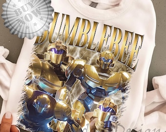 May include: White sweatshirt featuring a graphic of the word "BUMBLEBEE" in gold lettering above a design of gold and blue robots with lightning effects. The design is centered on the front of the sweatshirt.