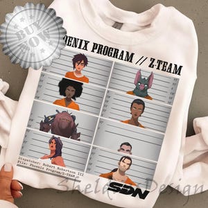 Puede incluir: Sudadera blanca con un gráfico de fotos de personajes y el texto "PHENIX PROGRAM // Z-TEAM". El diseño incluye un gráfico de "COMPRAR AHORA" en la esquina superior izquierda.