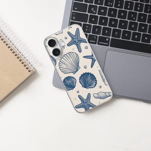 May include: A phone case with a cream background featuring a blue seashell and starfish pattern. The phone case is resting on a laptop, with a spiral notebook to the left. The laptop keyboard is visible.