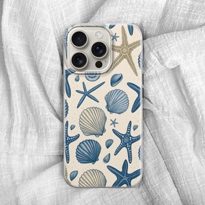 May include: A phone case featuring a cream-colored background with a pattern of blue starfish, seashells, and small shells. The case has a clear camera lens area and a protective bumper.