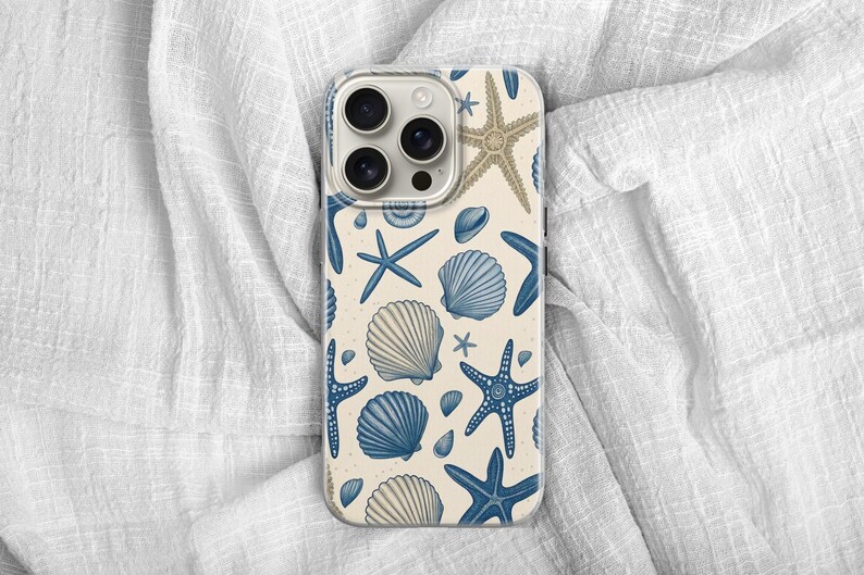 May include: A phone case featuring a cream-colored background with a pattern of blue starfish, seashells, and small shells. The case has a clear camera lens area and a protective bumper.