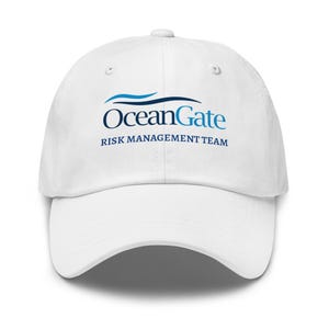 以下が含まれることがあります： 青色のOceanGateロゴが入った白い野球帽。ロゴには「OceanGate」の文字と「RISK MANAGEMENT TEAM」の文字が濃い青色のフォントで含まれています。帽子には湾曲したつばと上部にボタンが付いています。
