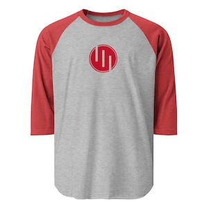 May include: A gray baseball-style shirt with red sleeves and a red crew neck. The shirt features a red circular logo with three vertical lines inside.