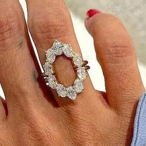 Könnte beinhalten: Ein Goldring mit einem Heiligenschein aus birnenförmigen Steinen in ovaler Anordnung. Der Ring ist als Ringwächter oder Enhancer konzipiert, mit einem offenen Mittelraum, der dazu dient, einen anderen Ring zu umrahmen, mit polierter Metallschiene.