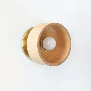 May include: A round wooden wall sconce with a brass backplate and a single light bulb.