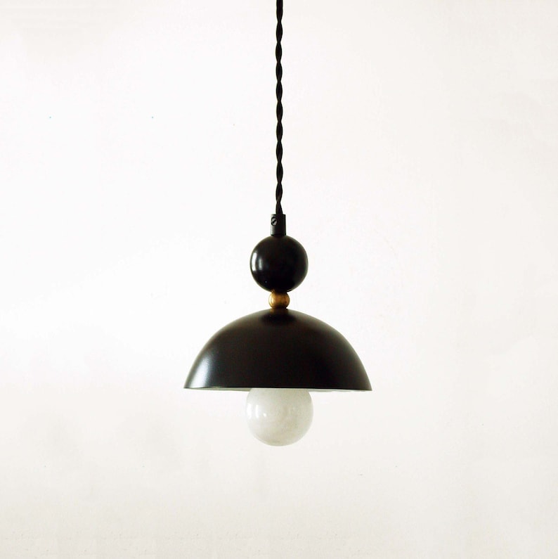 May include: A black pendant light with a round, white globe bulb. The light fixture has a black, dome-shaped shade and a black cord with gold accents.
